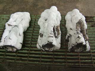 Molds filled with bronze. Ceramic shell molds are filled with dark metal. Some cooled splashes of metal are also visible on parts of the molds.