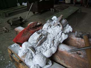 First Glimpse The Ceramic shell has been chipped away from the casting enough to see that the figure has been captured in bronze. The tools used are shown nearby (a small block hammer, a cold chisel, and a pnuematic chisel.