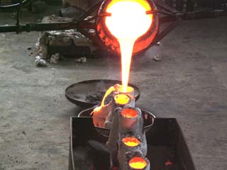 Crusible of molten bronze Crusible of bright yellow molten bronze is being poored into molds. Previously poored molds glow with cooling metal in the foreground.